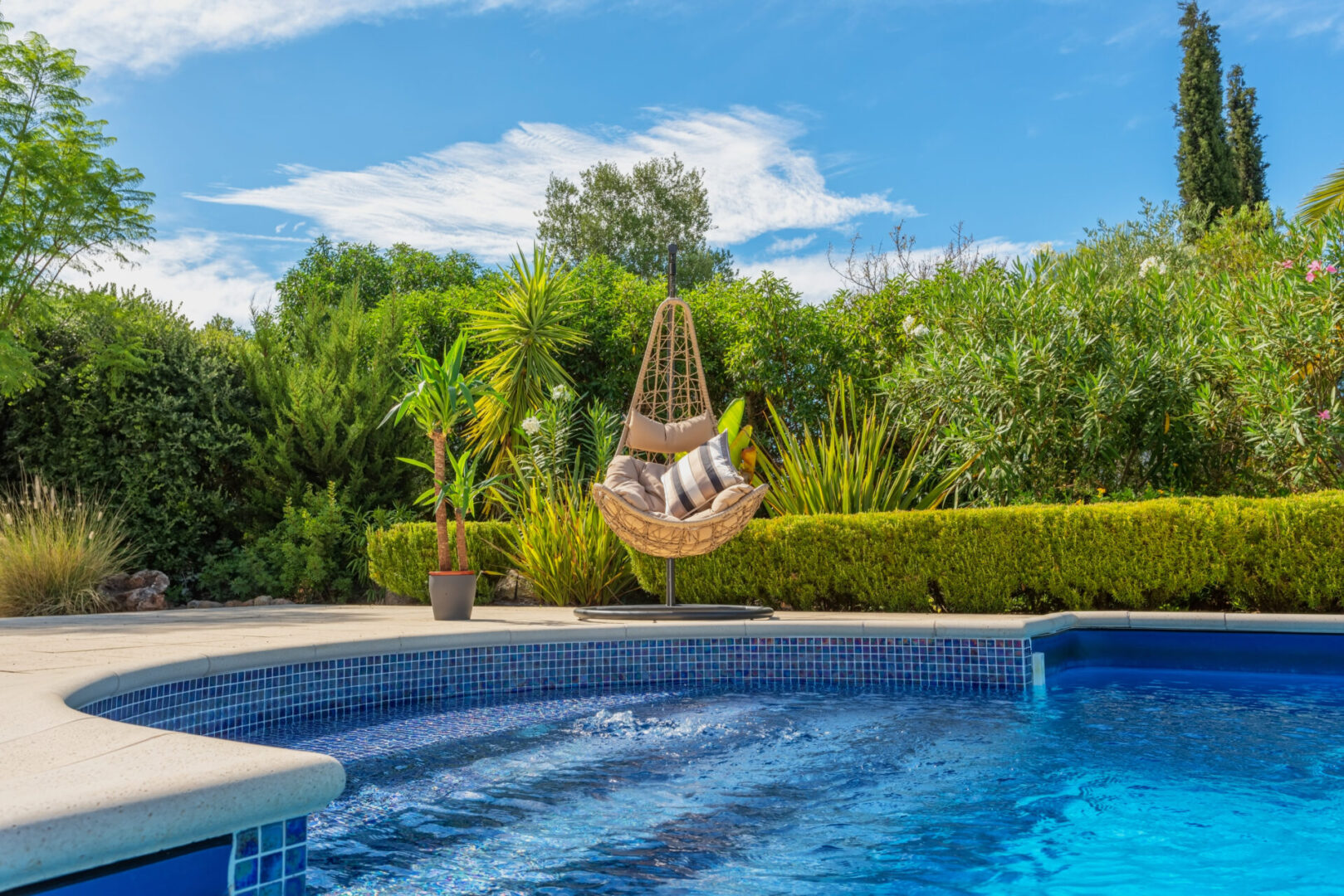 Luxurious pool in the garden of a private villa, hanging chair with pillows for leisure tourists, in summer. Portugal, Algarve